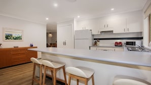 Una cocina moderna con armarios blancos, una isla grande con taburetes de bar y un área de comedor visible a través de un arco.