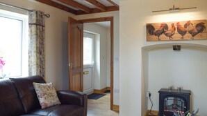 A living room with a brown leather sofa, a wooden door, a black wood-burning stove, and a painting of roosters on the wall.