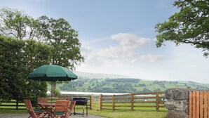 An outdoor patio with a table and chairs, a grill, and a view of rolling hills.