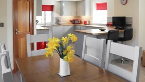 A modern kitchen with white cabinets, a red microwave, and a dining area with a white table and chairs.