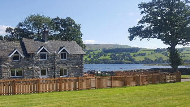 A stone house with a wooden fence, a grassy lawn, and a lake view.