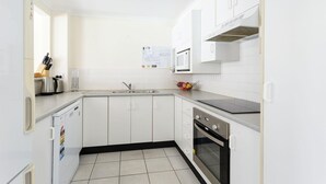 Cocina compacta con armarios blancos, pileta de acero inoxidable, microondas, estufa y refrigerador.
