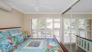 Ein Schlafzimmer mit einem Bett, einem Deckenventilator und Blick ins Freie durch große Fenster.