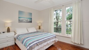 A bedroom with a bed, two bedside tables, a nightstand, a painting, and a window with curtains. - Beach Shack - close to the beach (Hawks Nest)