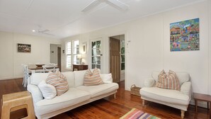 A spacious living room with a large white sofa, a smaller sofa, and a dining area with a table and chairs. - Beach Shack - close to the beach (Hawks Nest)