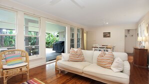 A spacious living area with a white sofa, striped cushions, a wicker chair, and a dining table. - Beach Shack - close to the beach (Hawks Nest)