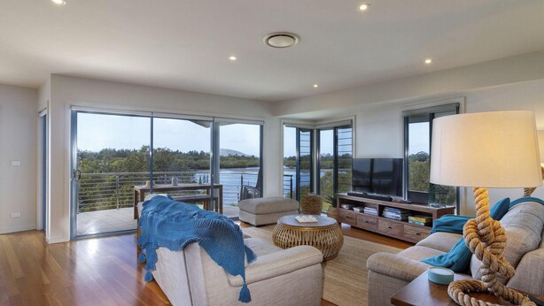 A spacious living room with a large TV, comfortable seating, and a balcony with a scenic view. - Myall River Magic - well-appointed townhouse overlooking the Myall River (Tea Gardens)