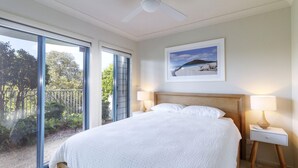 A bedroom with a large bed, two bedside tables with lamps, a ceiling fan, a large window with a view of greenery, and a framed picture on the wall. - Myall River Magic - well-appointed townhouse overlooking the Myall River (Tea Gardens)