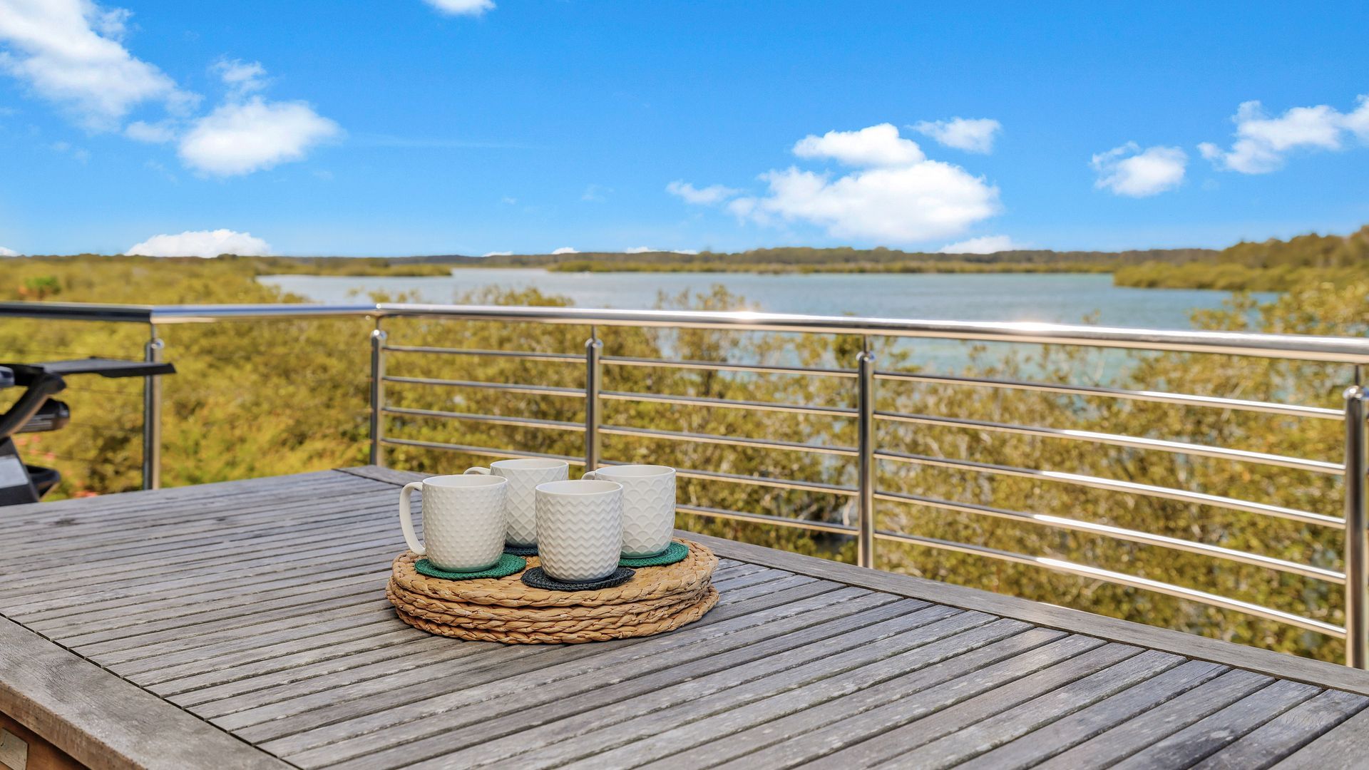 Een houten terras met een metalen hekwerk met uitzicht op een wateroppervlak en een landschap in de verte.