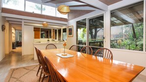 A spacious dining area with a wooden table and chairs, large windows offering a view of the garden, and a modern kitchen in the background. - Sandy Shores - Hawks Nest Holiday Home (Hawks Nest)