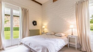 Een slaapkamer met een groot bed, twee nachtkastjes met lampen, een radiator en uitzicht op een tuin door een schuifdeur.