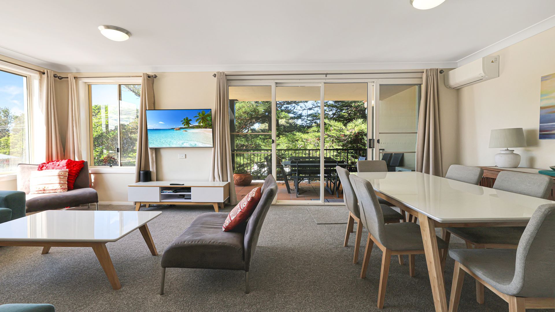 A hotel room with a seating area, a dining table, and a TV displaying a tropical beach scene.