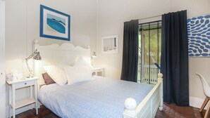 Un dormitorio con cama, mesitas de noche, escritorio, silla y ventana con cortinas.