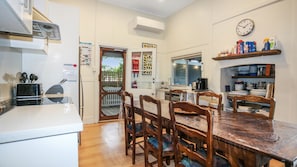 Une cuisine compacte avec une table à manger en bois, des chaises, une machine à café et une horloge au mur.
