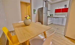 Cozy living space with a dining area and kitchenette, featuring a wooden table and chairs, a vase with flowers, and a refrigerator.