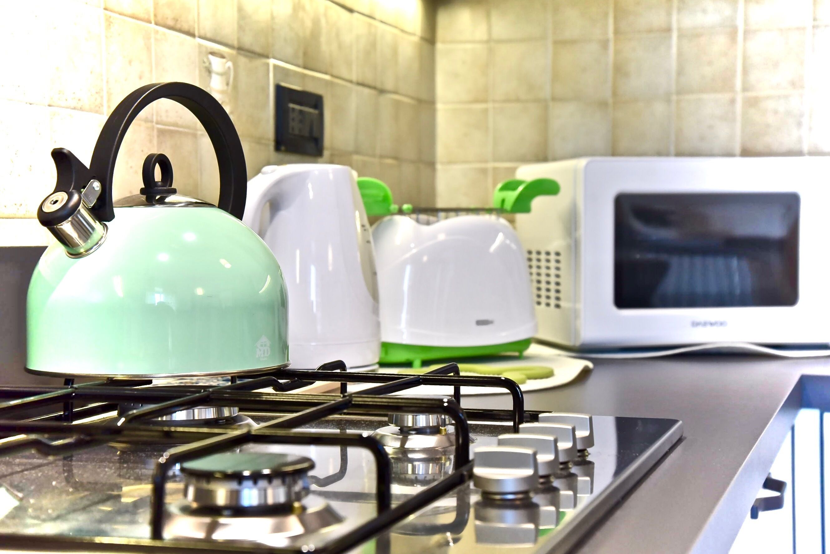 A kitchen with a gas stove, a green kettle, a white toaster, and a microwave.