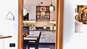 A modern kitchen with light wood cabinets, a hanging pendant light, and a dining area with a table and chairs. - Modern apartment between Milan and Como (Cogliate)