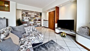 A modern living room with a sofa, a television, and a bookshelf filled with books and decorative items. - Modern apartment between Milan and Como (Cogliate)