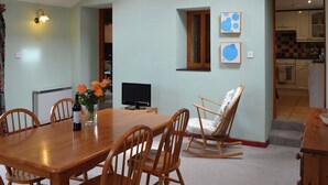 Un'area pranzo con tavolo in legno, sedie, televisore e un vaso con fiori.