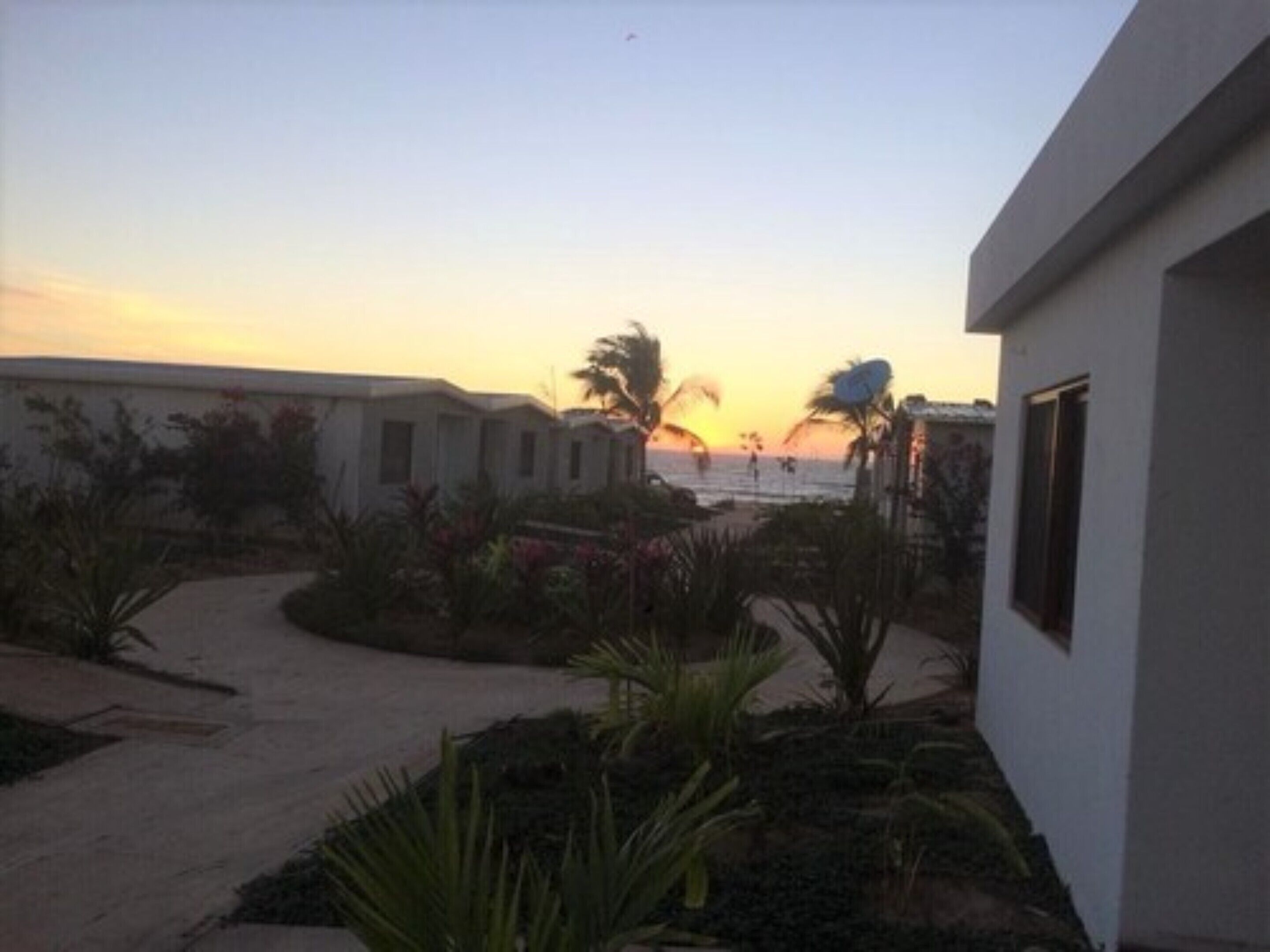 Un sendero que lleva a un edificio con vista al atardecer sobre el océano.