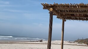 Eine Holzkonstruktion am Strand mit einem Reetdach, vor einer Küstenlandschaft.