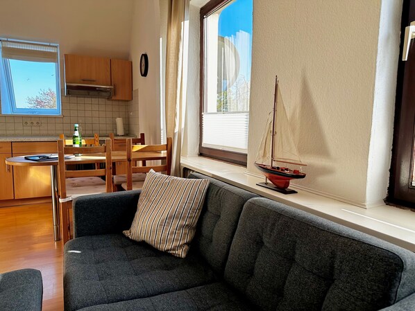 A cozy living room with a dark grey sofa, a striped pillow, and a small sailboat model on a windowsill.