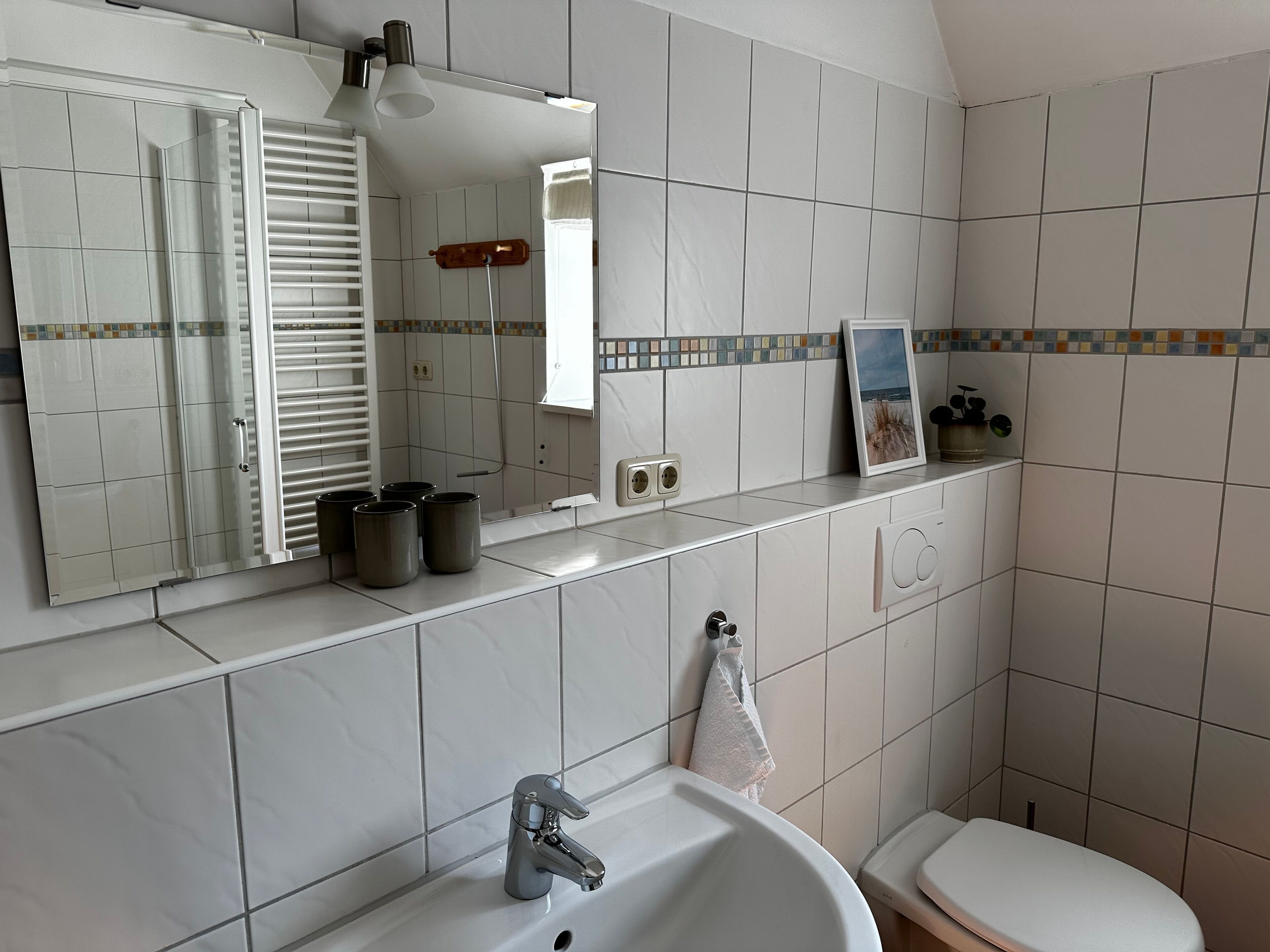 A bathroom with a white sink, a mirror, a towel hanging on the wall, and a toilet.