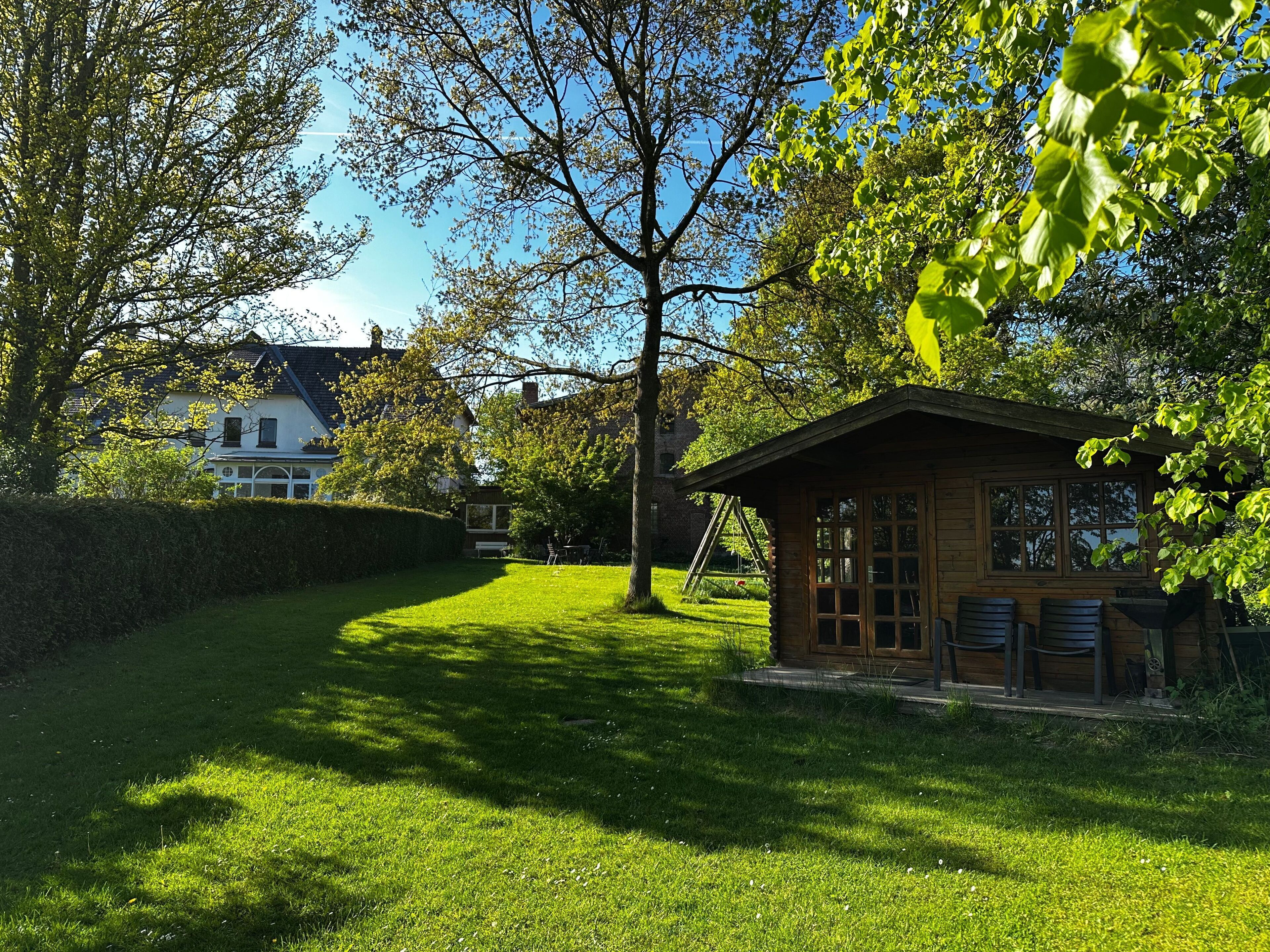 A small wooden cabin with a window and a door, surrounded by a well-maintained lawn and trees.