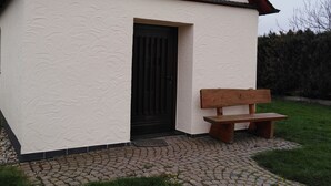 Een klein gebouw met een kruis bovenop, de cijfers 1853, en een bank ervoor.
