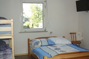 Ein Schlafzimmer mit einem Einzelbett, einem Fenster, einem Holzstuhl und einem an der Wand befestigten Fernseher.