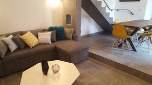 Een moderne woonkamer met een bruine modulaire bank, een witte salontafel en een eethoek met gele stoelen.