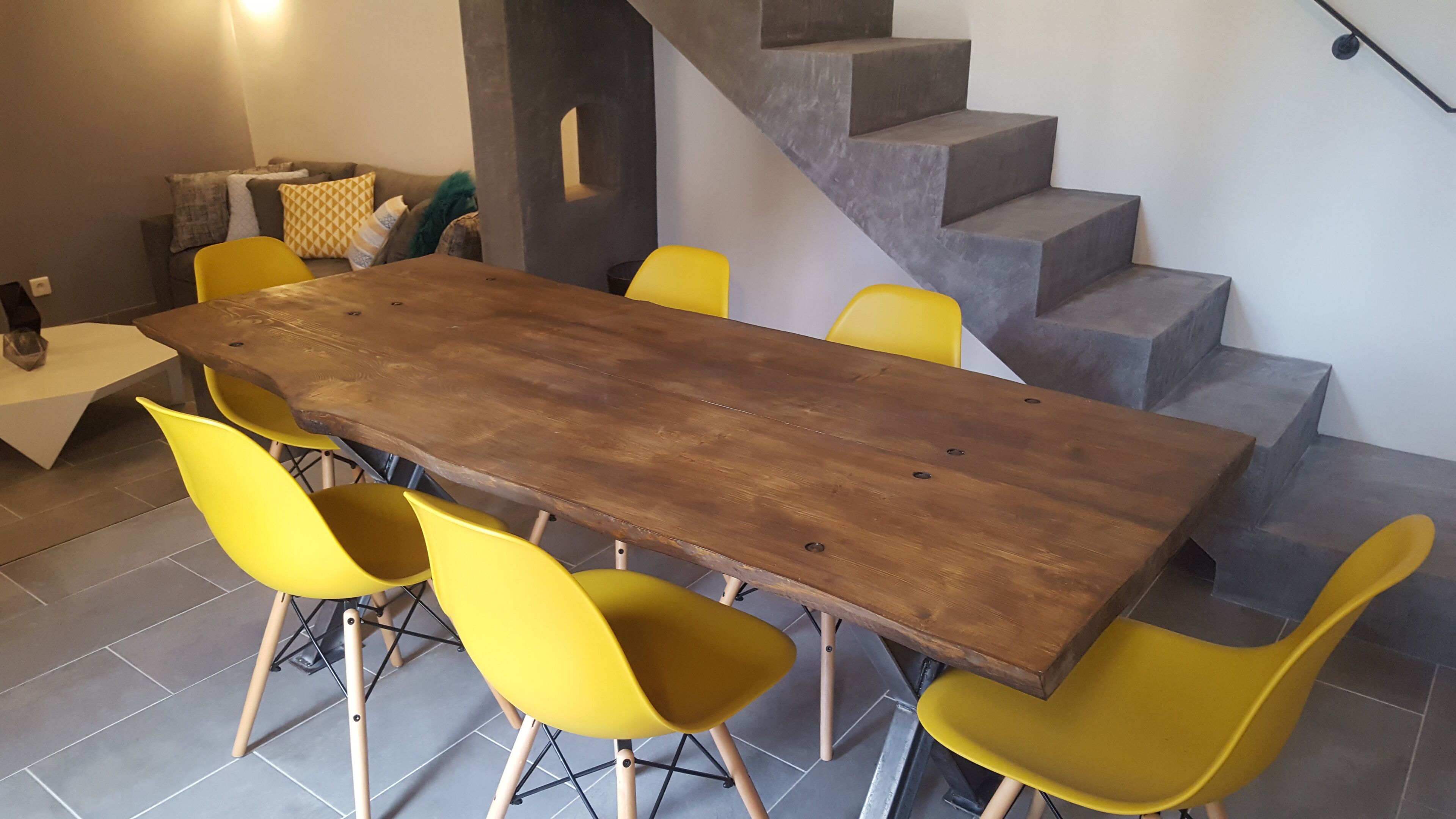 A dining area with a long wooden table and yellow chairs, a staircase, and a modern interior design.