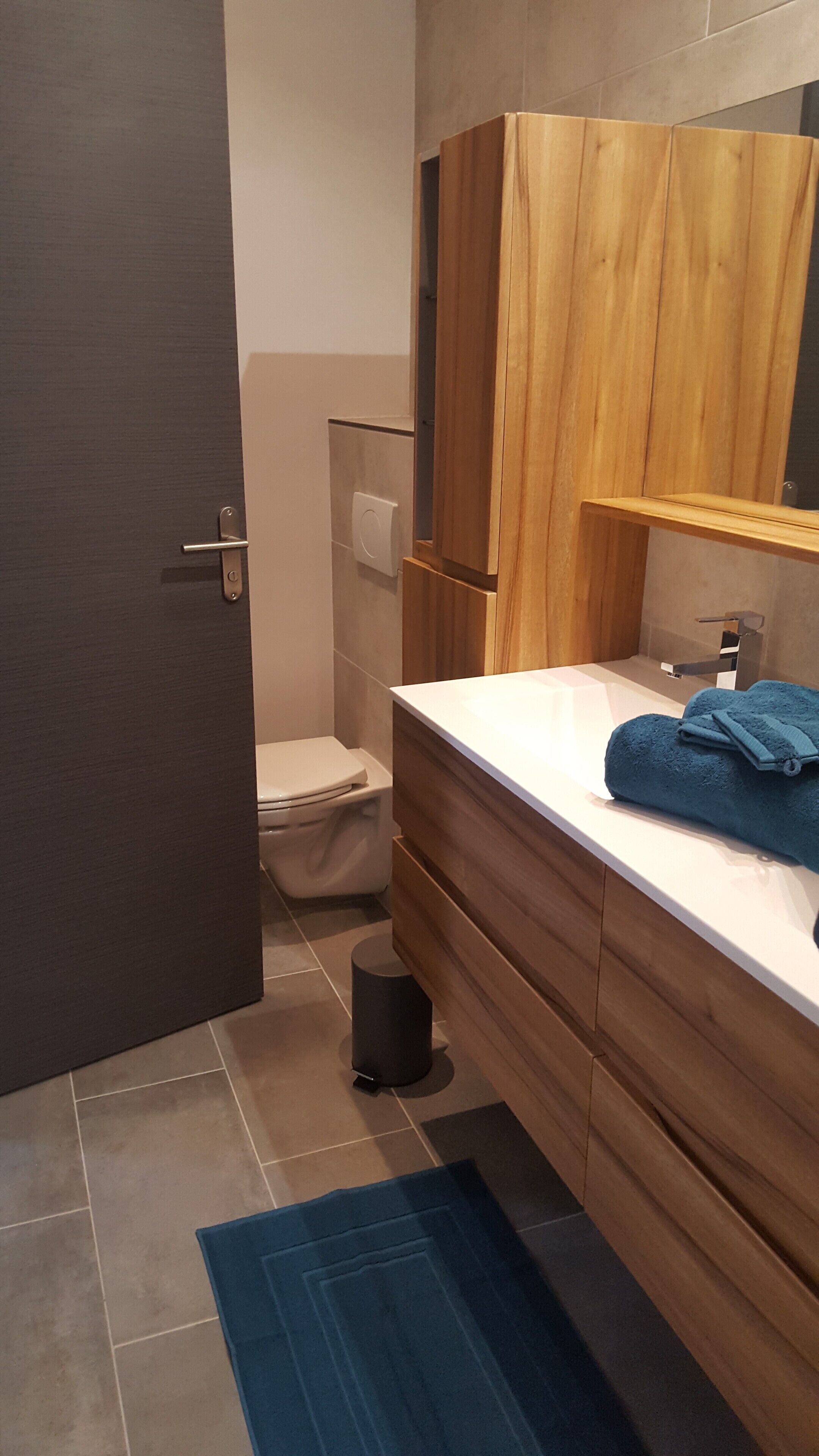 A modern bathroom with a wooden vanity, a white sink, and a blue towel.