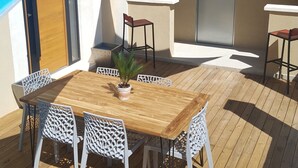 Een houten terras met een tafel, stoelen, een bloempot en een deur met een bordje.
