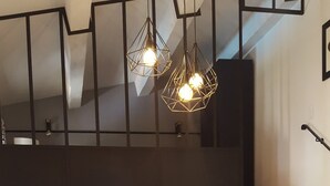 Een eetgedeelte met een houten tafel en gele stoelen, een trap en hangende geometrische lampen.