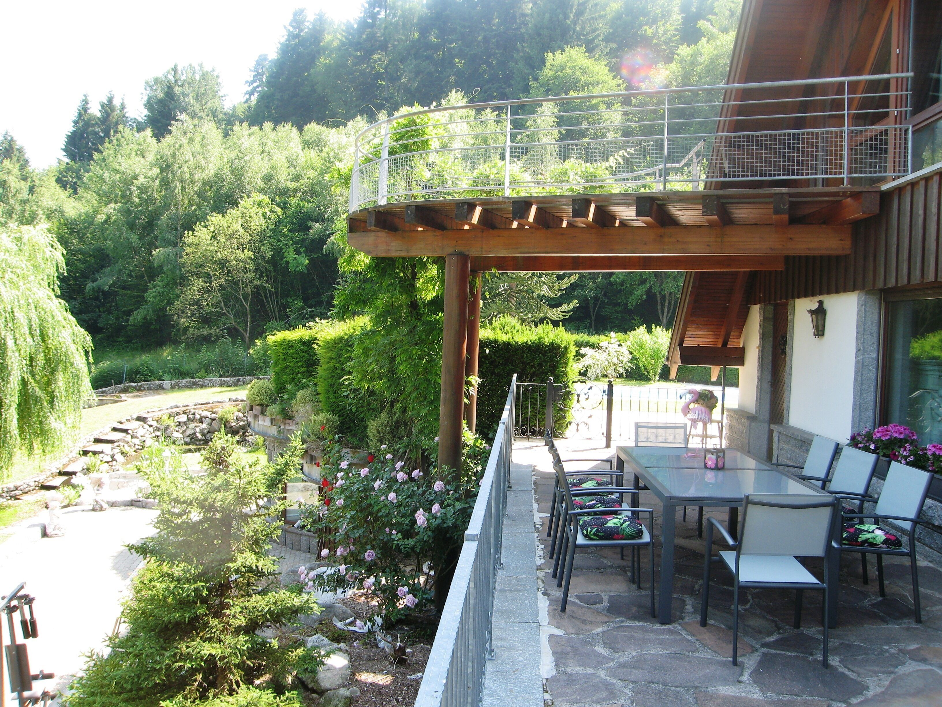 Une terrasse avec une table et des chaises, entourée d’un jardin où poussent différentes plantes et fleurs.
