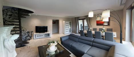 En moderne stue med en grå sofa, et sort sofabord, et fjernsyn og en trappe med gelænder.