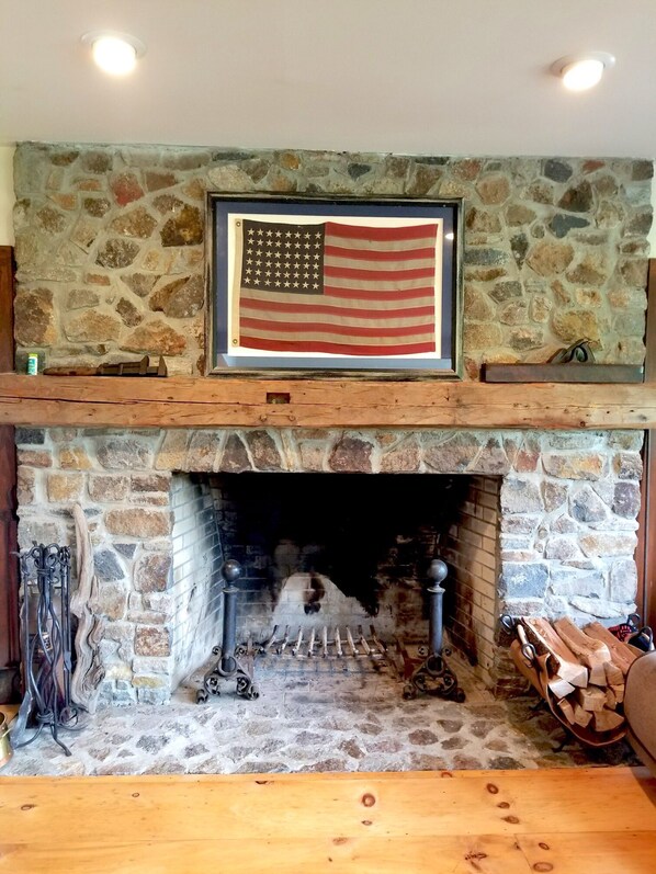 Una chimenea de piedra con una bandera estadounidense en la parte superior, un fuste de madera y un interior rústico.