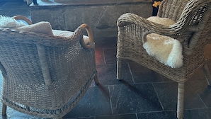 A fireplace with a fire, two wicker chairs with fluffy cushions, and a stone fireplace surround. - Hallingskarvet Fjellstue AS (Hol)