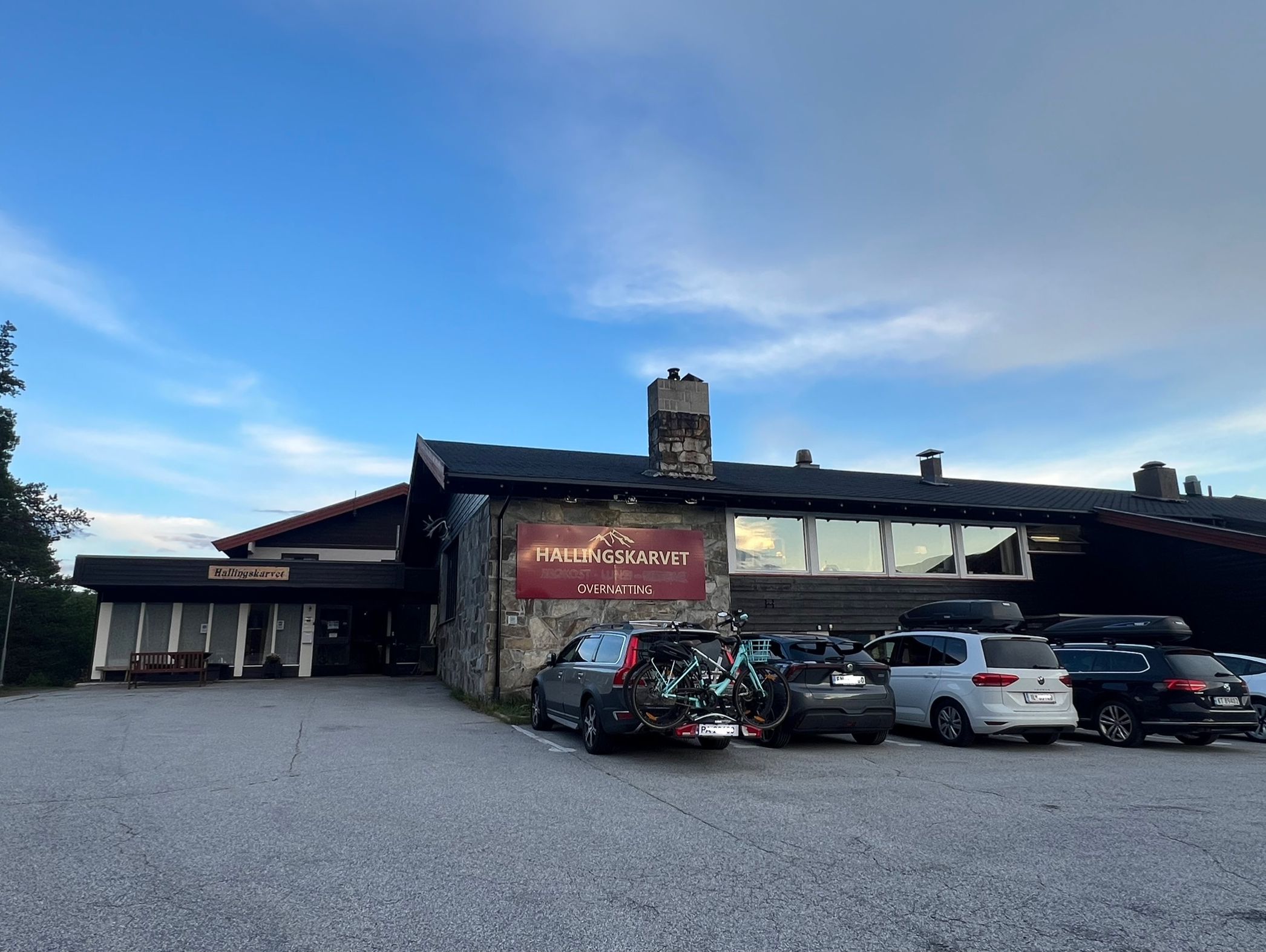 Un bâtiment sur lequel on peut lire l’inscription « HALLINGSKARVET OVERNATTING ». Des voitures et des vélos sont garés devant.