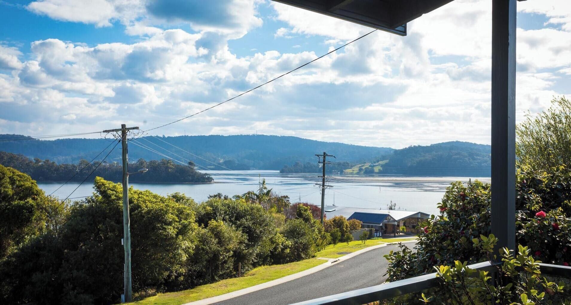 A residential area with a road leading to a bridge over a lake, surrounded by greenery and hills.