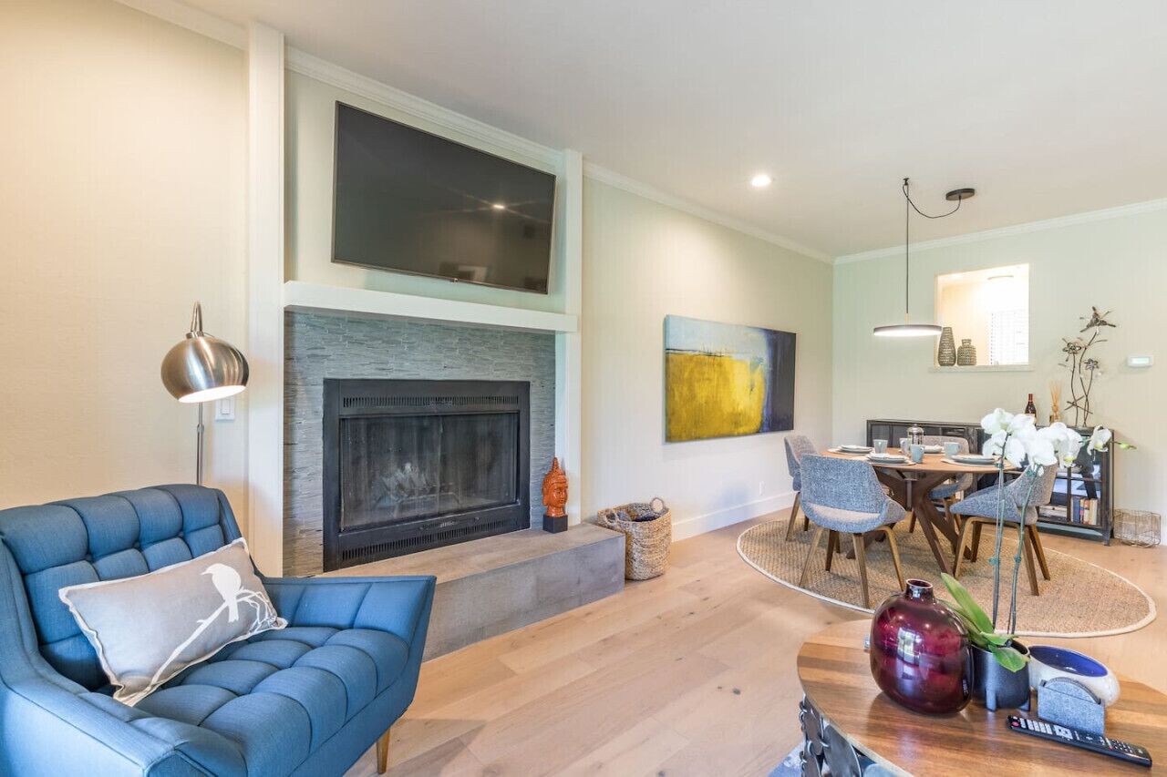 Una sala de estar moderna con chimenea, un sofá azul, comedor y plantas decorativas.