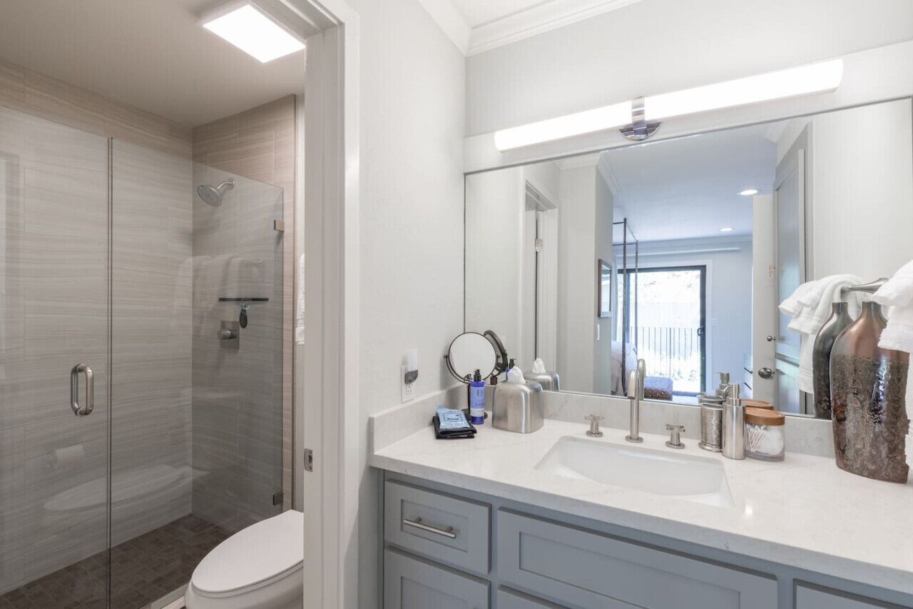 Un baño moderno con cabina de ducha de vidrio, un espejo grande y un lavabo blanco con artículos de aseo.