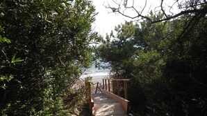 Un chemin en béton mène à une terrasse en bois d’où l’on a vue sur la plage.