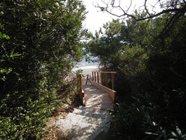 Ein Betonweg führt zu einer Holzterrasse mit Blick auf den Strand.