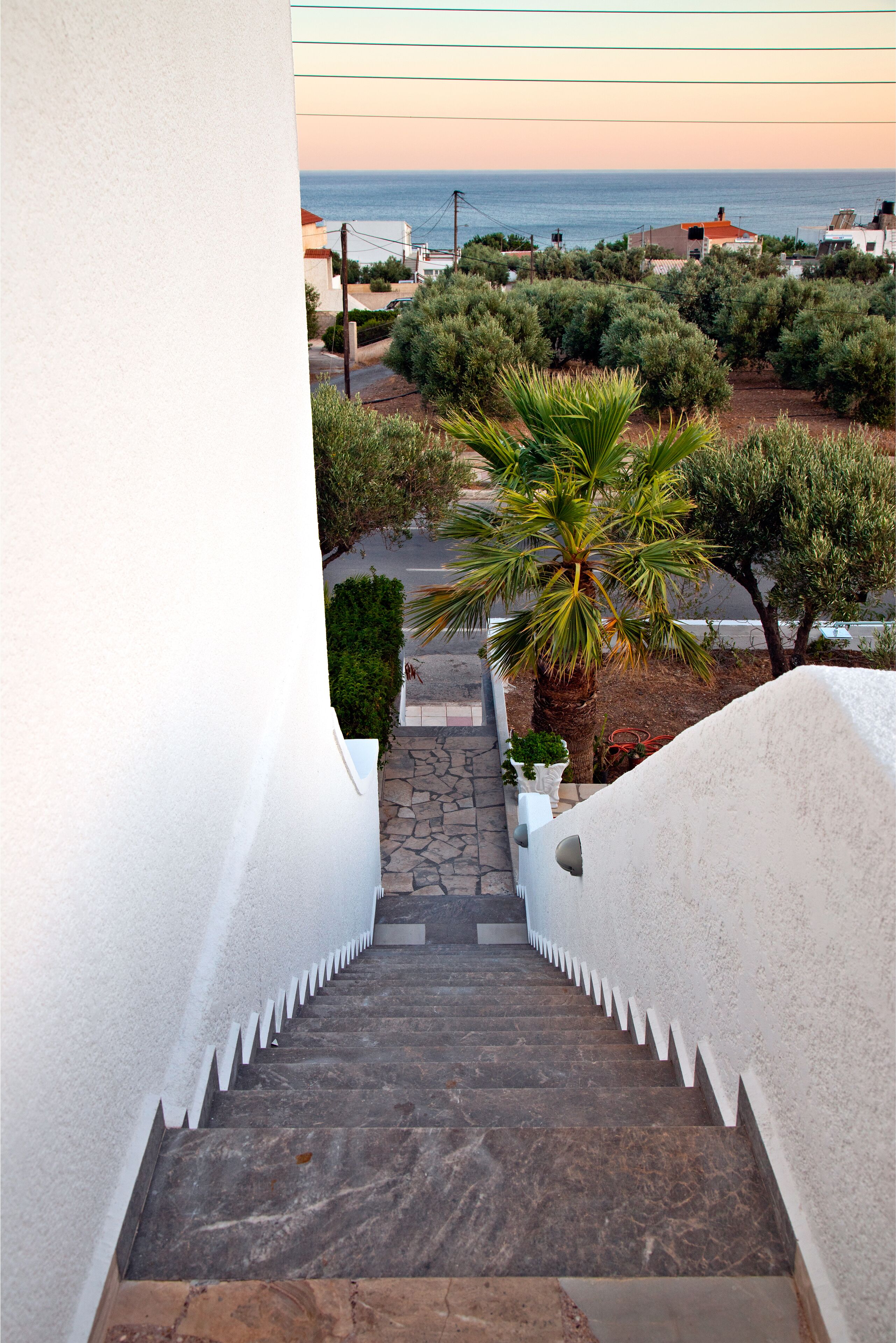 Una escalera lleva a un balcón con vista a una zona costera con casas y vegetación.