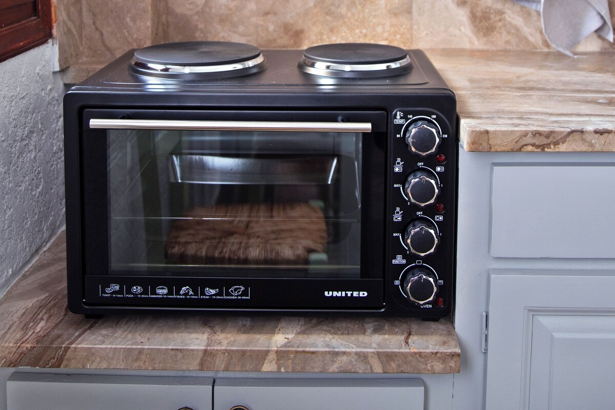 A compact kitchen with a built-in oven and microwave, a white range hood, and a marble backsplash.