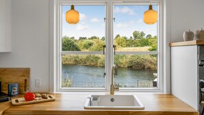 Una cocina con un lavamanos doble, encimera de madera y vistas a un río a través de un ventanal grande.