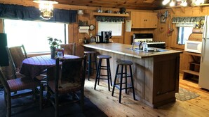 A cozy cabin-style kitchen with a wooden island, bar stools, a dining table with chairs, and a refrigerator.