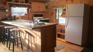 A wooden cabin kitchen with a central island, bar stools, a refrigerator, and a stove.